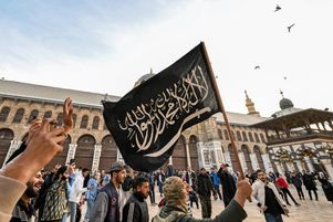 Un combattant rebelle syrien tient un drapeau noir islamiste dans une mosquée omeyyade à Damas, le 10 décembre 2024. 