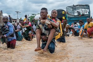 Un habitant porte une femme tandis que d’autres pataugent dans les eaux de crue dans le quartier de Ndjili à Kinshasa (RD-Congo), le 6 avril. 